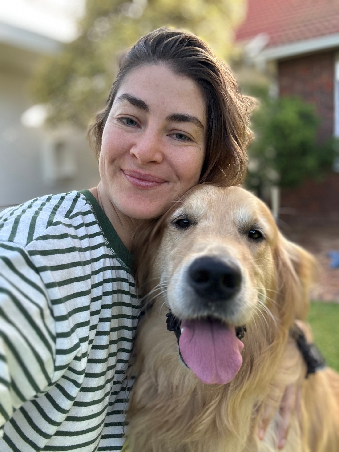 Golden retriever grinning next to their human in the garden